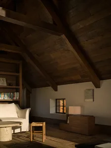 Cozy attic living room featuring reclaimed wood cathedral ceiling, white linen sofa, stone coffee table, and wooden stool in warm natural light.