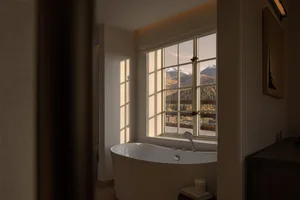 A serene bathroom featuring a white freestanding bathtub positioned in front of a large multi-pane window with a breathtaking view of snow-capped mountains and autumn forest.