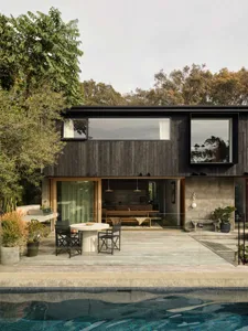 Modern two-story villa with dark charred wood facade, large glass windows, outdoor dining area with round table and black chairs, and a swimming pool in the foreground.