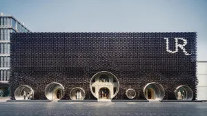 Front view of Urban Revivo flagship store in Taipei featuring a massive black textured façade made of recycled plastic tiles and multiple circular tube-shaped entrances with mannequins displayed inside.