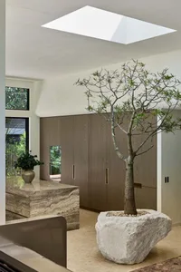 Modern minimalist entryway featuring a large travertine stone console, a massive natural rock planter with a living tree, light wood cabinetry, and a skylight above.
