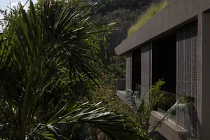 Modern concrete house with perforated metal screens and a living green roof nestled into a tropical hillside surrounded by lush palm trees.