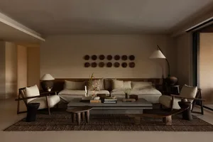 Modern organic living room featuring a low-profile beige sofa, sculptural dark wood armchairs, a large stone coffee table, layered natural fiber rugs, and circular wood wall art under warm ambient lighting.