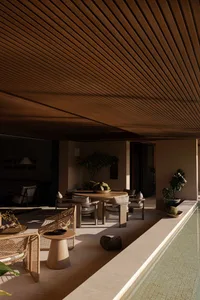 Luxurious covered outdoor patio featuring a round teak dining table, woven rattan lounge chairs, concrete side tables, and a long reflecting pool under a dramatic wood slat ceiling.