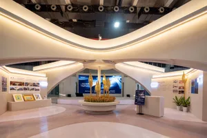 Modern exhibition hall interior with dramatic curved white plaster ceiling, integrated LED cove lighting, central circular installation with golden woven sculptures, and exhibition panels along the walls.