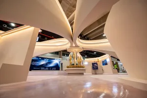 現代展覽攤位以白色流線型曲面天花板為主體，搭配整合式照明與中央懸吊金色裝置。
