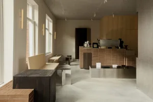 Minimalist cafe interior featuring a long light-wood bench, dark wood block seating, a brown tiled coffee bar with stainless steel espresso machine, and large windows with brick wall detail.