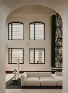 Modern minimalist living room featuring a large arched entryway, off-white modular sofa, dark marble accent wall, and four arched windows with black blinds.