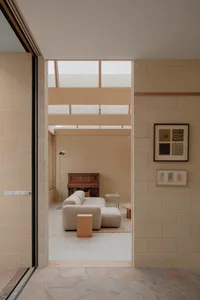 View into a minimalist living room featuring light-colored concrete block walls, a large modular beige sofa on terrazzo flooring, wooden accents, and high clerestory windows allowing soft natural light.