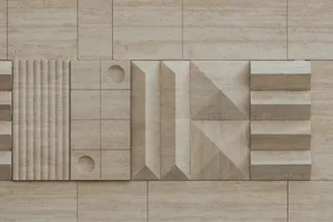 Close-up of a beige travertine stone wall featuring various three-dimensional geometric patterns including fluted columns, circular cutouts, angular pyramids, and stepped reliefs.