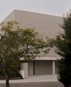 Exterior view of a brutalist concrete building with a strong geometric form, overhanging canopy, and surrounding trees under an overcast sky.