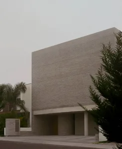 Exterior view of a brutalist concrete brick building with a large overhanging rectangular volume and wooden entrance door.