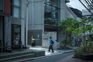 Modern minimalist concrete cafe facade with a woman in a green vest standing at the counter and a pedestrian walking by on a quiet Taipei street.