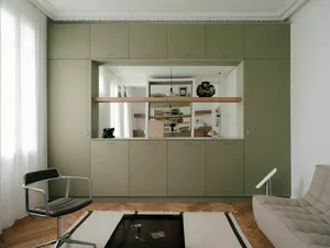 Modern living room with sage green built-in cabinetry, herringbone parquet floor, black leather swivel chair, and light grey sofa