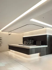 Modern minimalist cafe interior featuring a long dark wood service counter with white stone top, underlit with warm LED lighting, white tiled floor, and dramatic linear ceiling lights.