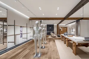 Modern minimalist lifestyle showroom interior with light oak wood flooring, white abstract mannequins, long wooden display tables, and warm linear lighting.