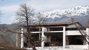 Modern white stucco mountain villa with wooden details, set against a dramatic backdrop of snow-covered mountains in winter.