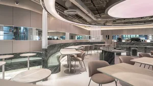Modern cafe interior with dark green marble curved banquette seating, light marble tables, and neutral upholstered chairs in a spacious, bright layout.