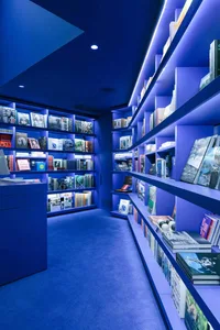 Immersive monochromatic blue library room with floor-to-ceiling LED backlit bookshelves and deep blue carpet.