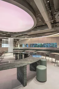 Modern restaurant interior featuring a long curved green marble counter, matching stools, upholstered dining chairs, and a massive circular pink illuminated ceiling installation.