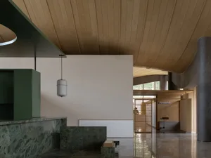 Modern commercial reception area featuring a dramatic curved wooden ceiling, green marble counter, and minimalist beige walls with pendant lighting.