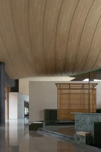 Modern lobby interior featuring a dramatic curved wooden ceiling, green marble reception desk and steps, wooden lattice screen, and polished reflective floors.
