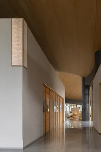 Modern minimalist hallway with curved wooden ceiling, textured stone walls, wooden slat doors, and reflective polished floors.