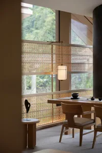 Modern Japanese-style dining area featuring solid oak table and chairs, rattan woven window screens, cylindrical pendant lamp, and a scenic mountain view through large windows.