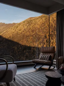 Modern lounge chair with cognac leather and striped cushion placed in front of a huge window revealing a vast mountain covered in golden autumn forest