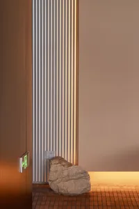 Modern minimalist entryway featuring a large natural stone sculpture, vertically fluted wooden wall with integrated warm lighting, terracotta tile floor, and a glowing green exit sign.
