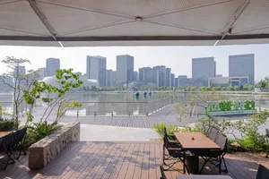 Modern wooden terrace with dining table and chairs overlooking a lake and the Songshan district city skyline in Taipei, with lush greenery in the foreground.