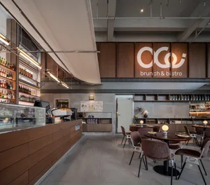 Modern brunch bistro interior with walnut wood counter, brown velvet chairs, round dining tables, and large illuminated logo on the back wall.