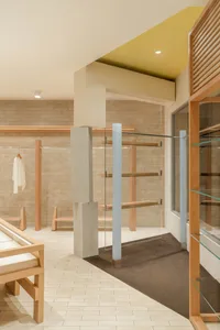 現代極簡精品店內部，設有淺橡木服裝展示架、混凝土結構柱、米色磚牆，以及溫暖的黃色天花板重點。