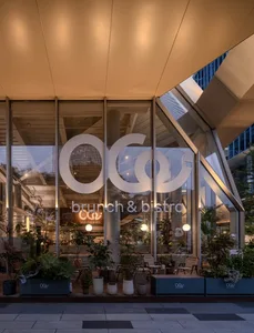 Evening view of Oao Brunch & Bistro modern glass facade with large white circular logo, abundant potted plants, and warm interior lighting in Taipei.