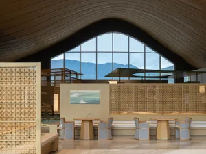 Modern Japanese-style lounge with curved wooden ceiling, light wood furniture, lattice screens, and large arched windows overlooking misty mountains.