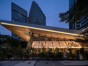 Modern glass facade of OE Brunch & Bistro restaurant in Taipei at dusk, featuring a dramatic cantilevered illuminated canopy, abundant potted plants, and contemporary high-rise buildings in the background.