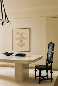 Ornate black carved baroque chair placed beside a glossy white marble dining table with abstract stone artwork on the wall