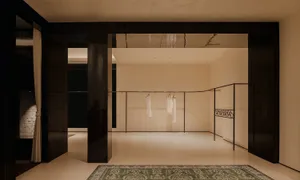 Modern minimalist dressing room featuring dark wood architectural panels, a green Persian-style rug, and elegant clothing racks with white garments hanging.