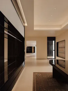 Modern minimalist hallway featuring a glossy dark wood built-in cabinet on the left, a curved dark wood console table on the right, a vintage Persian rug on light tile flooring, and recessed ceiling lighting.