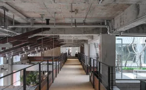 Long double-height industrial corridor with exposed concrete walls, weathered steel beams, black metal railings, and pendant lighting in a modern loft space.