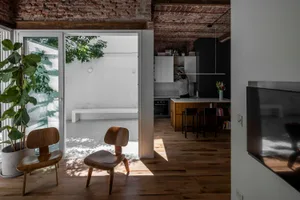 採光充足的開放式 loft 室內空間，兩張木質 Eames 椅、大型琴葉榕盆栽、裸露紅磚天花板，以及可看見木質中島的現代廚房。