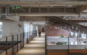 Long perspective view of an industrial-style mezzanine corridor in a creative cultural park, featuring exposed concrete walls, wooden paneling, metal railings, and a person walking toward the background.