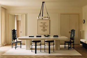 Modern minimalist dining room featuring a large cream marble table, two black modern dining chairs, and two ornate black baroque-style armchairs, with a large abstract painting and a modern circular chandelier.