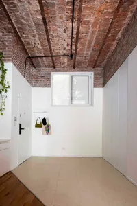 Modern minimalist entryway featuring an exposed red brick ceiling, white walls, light beige tiled floor, and white oak flooring transition.