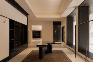 Modern minimalist hallway featuring a curved ebony console table, built-in dark wood cabinetry, a vintage Persian rug, and warm ambient lighting.