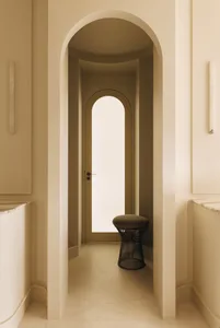 Minimalist entryway featuring consecutive arched niches in warm off-white plaster, with a black wireframe stool placed beneath the inner arch.