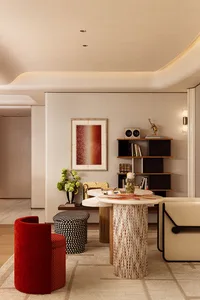 Modern living room featuring a bright red velvet tub chair, patterned ottoman, cylindrical marble and wood side table, and built-in shelving with art and decor.