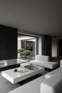 Modern minimalist living room featuring light grey modular sofas, a large white marble coffee table, black accent walls, and a view of a traditional Chinese courtyard with a bonsai tree.