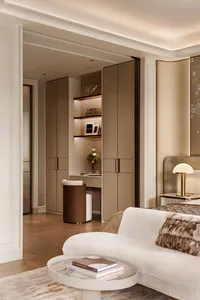 Modern luxury bedroom featuring a built-in illuminated vanity nook with floating shelves, neutral beige cabinetry, a curved white chaise lounge, and marble coffee table.