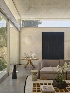 Modern minimalist living room featuring exposed concrete walls and ceiling, a beige oak-base sofa, round wooden coffee table, large black abstract painting, and a large white paper lantern pendant lamp.
